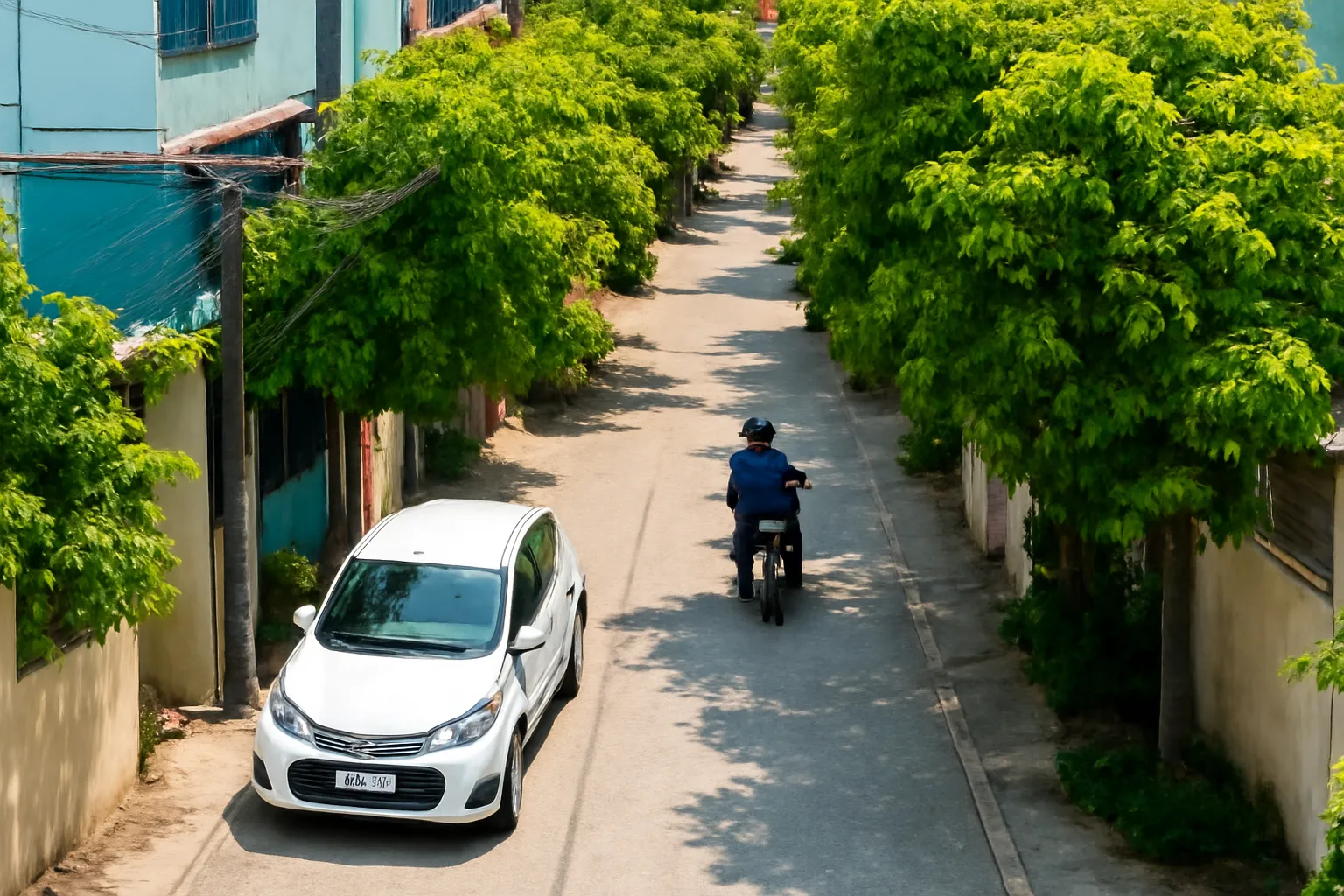 Hẻm nhỏ có cây xanh, người dắt xe máy vào, ô tô con đỗ ở đầu hẻm